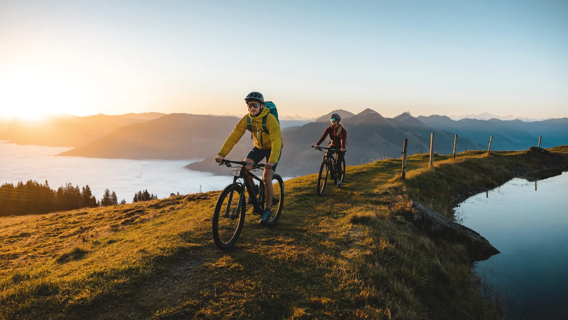 Zwei Radfahrer fahren auf einem schmalen Pfad am Brixental vorbei bei Sonnenuntergang.