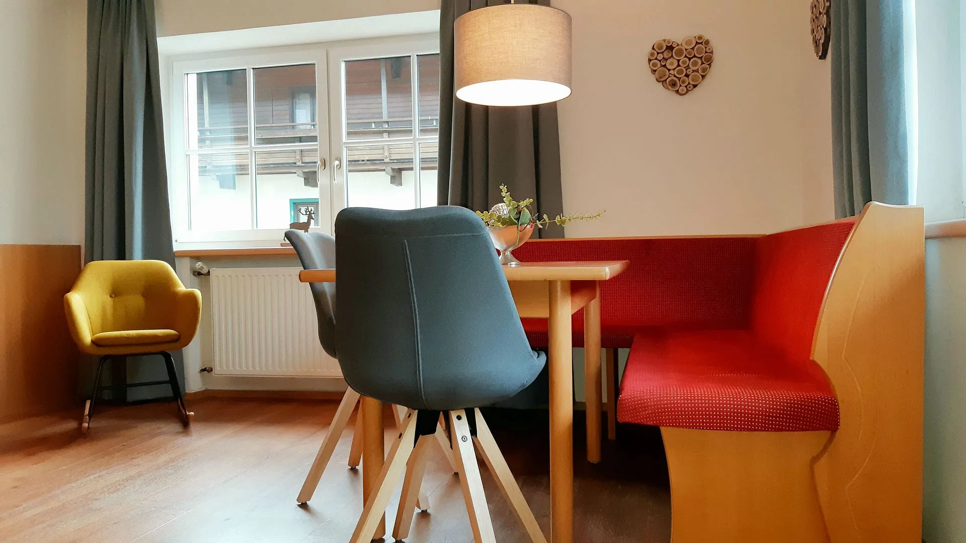 Gemütlicher Essbereich mit rundem Tisch, roter Sitzgelegenheit, gelbem Stuhl und Lampe.