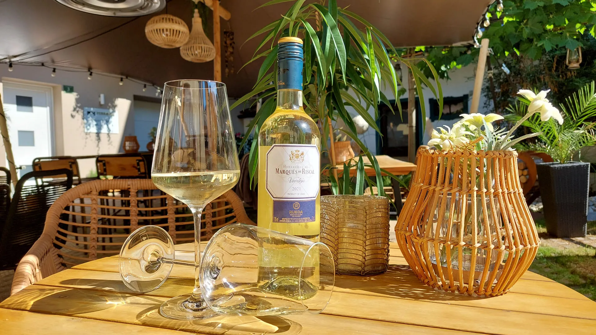Weißweinflasche und Glas auf einem Tisch, umgeben von Pflanzen.